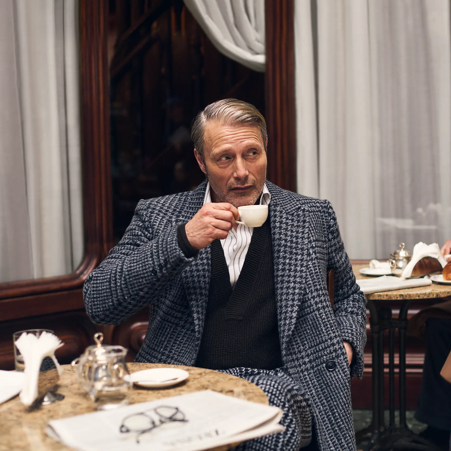 Mads Mikkelsen, seated in a café, wearing a Torino style tailored suit from the ZEGNA FW25 couture collection.