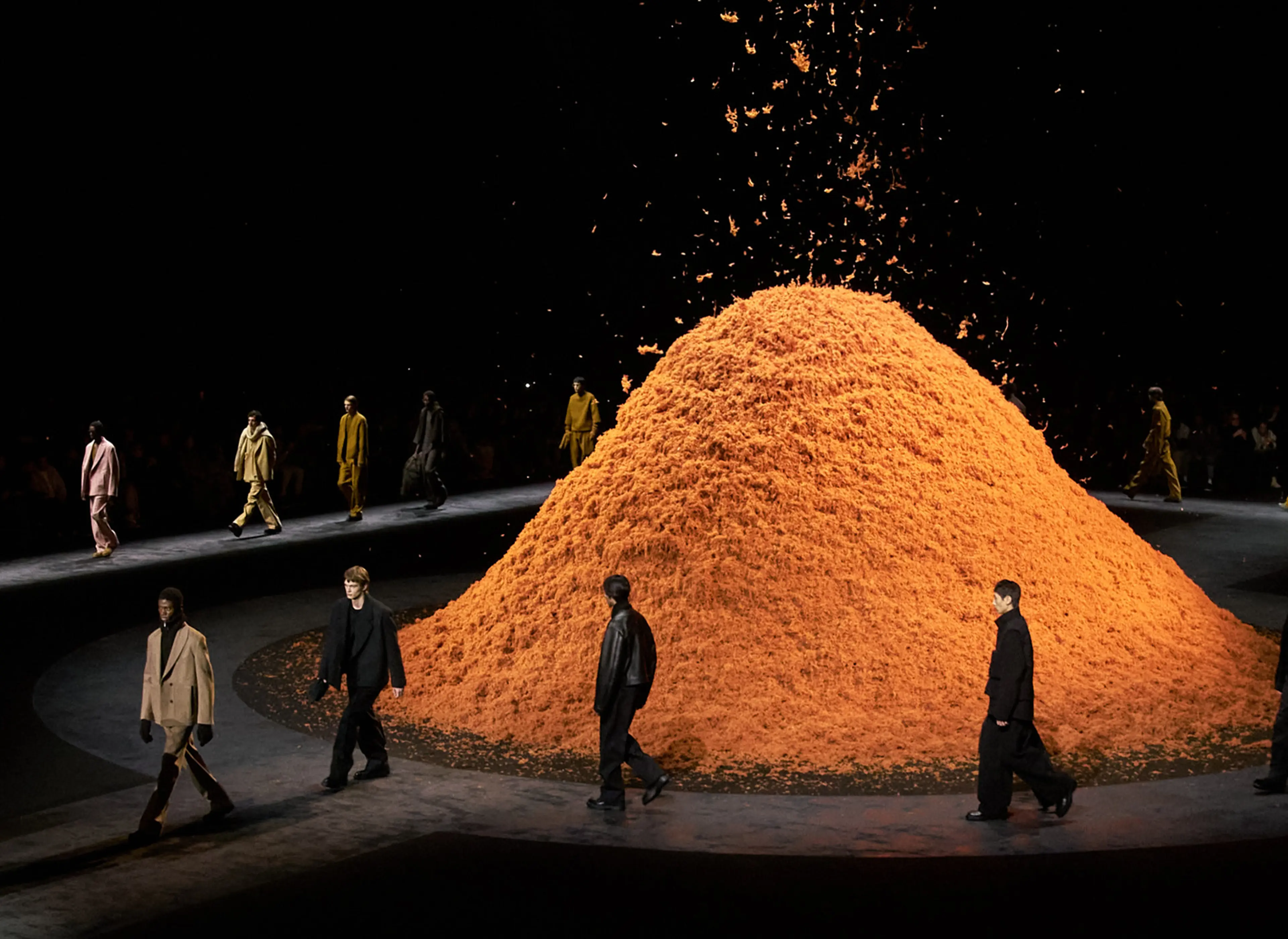 Models walking on the ZEGNA FW24 fashion show runway with a mountain of orange cashmere in the center.